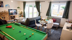 A pool table with balls, a sofa, a television, and a dining area with chairs and a table. - The Pines Villa 1 | Spacious 3BR | Cinema, Games & EV | Parking | Sleeps 10+ (West Northamptonshire)