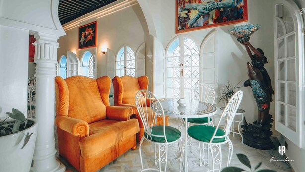 Una habitación con techo abovedado blanco, un sofá blanco con cojines verdes, una mesa redonda con sillas blancas y un cuadro sobre la mesa.