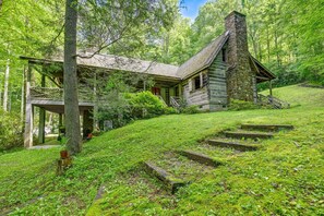 Eine rustikale Holzhütte mit einem Steinkamin, umgeben von üppigem Grün und einer Holzterrasse.