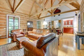 Ein geräumiges Blockhaus-Interieur mit einer großen Ledersofa, Holzbalken und einem Essbereich.