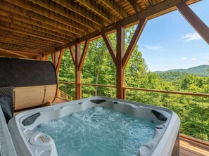 Ein Whirlpool mit einer Holzterrasse und Blick auf einen bewaldeten Gebirgszug.