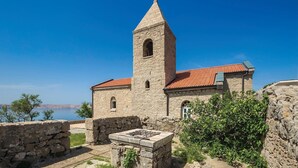 A stone church with a bell tower and a red-tiled roof, surrounded by greenery and a clear blue sky. - Nice home in Karlobag with WiFi (Karlobag)