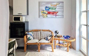 Ein gemütliches Zimmer mit einem Korbsessel, einem kleinen Beistelltisch und einem Bild von Booten an der Wand.