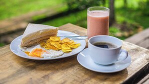 Eine Mahlzeit bestehend aus einem Sandwich, Eiern und Pommes auf einem Holztisch, dazu ein Smoothieglas und eine Tasse Kaffee.