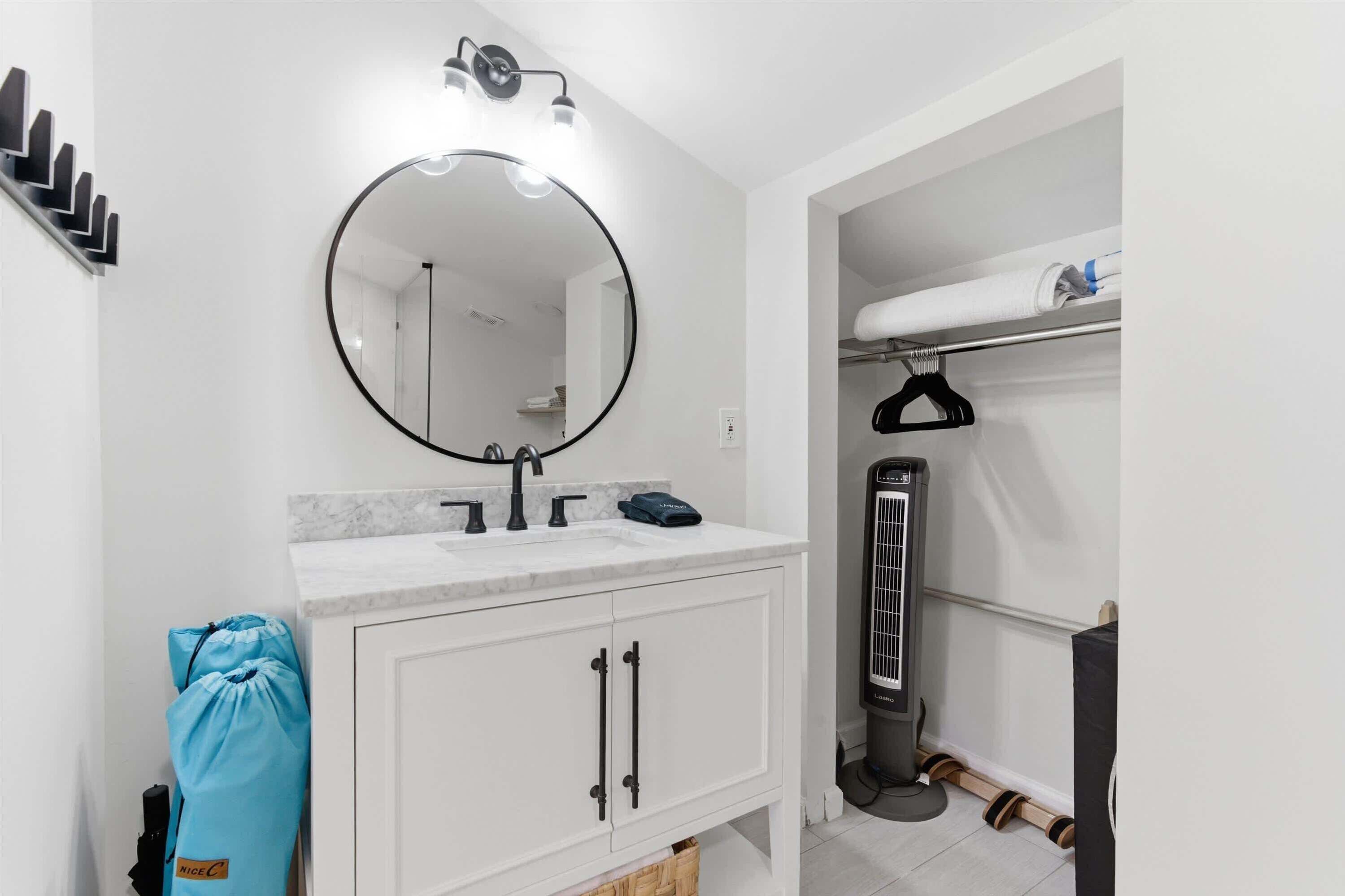 A modern bathroom with a round mirror, white cabinets, a marble countertop, and a towel rack.