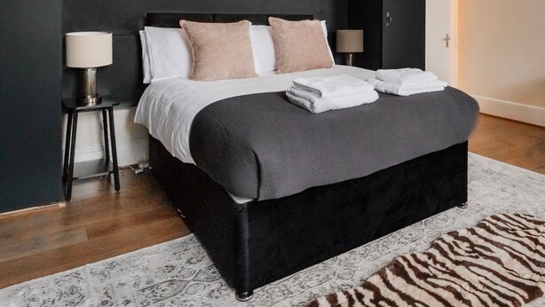 Un dormitorio moderno con una cama grande, armarios oscuros y una alfombra estampada.