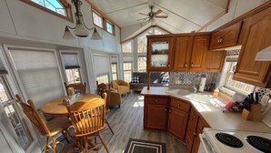Uma cozinha compacta com armários de madeira, uma área de refeições com mesa e cadeiras redondas, fogão e ventilador de teto.