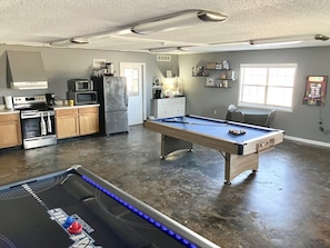 A spacious room with a pool table, kitchen area, and a pool table with lights.