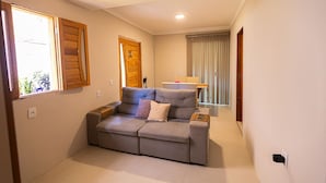 A living room with a grey sofa, wooden doors, and a window. - Casa com Piscina e Churrasqueira em Arembepe (Camaçari)