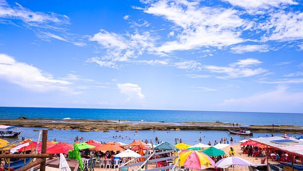 A beach with colorful umbrellas and boats. - Casa com Piscina e Churrasqueira em Arembepe (Camaçari)