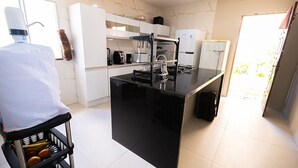 A modern kitchen with a black countertop, white cabinets, and a stainless steel sink. - Casa com Piscina e Churrasqueira em Arembepe (Camaçari)
