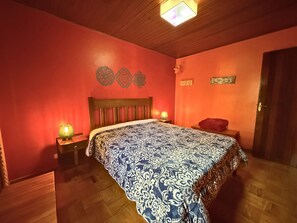 Une chambre à coucher avec une tête de lit en bois, une couvre-lit à motifs, deux lampes de chevet, un coussin rouge décoratif et un plancher en bois.