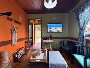 A cozy room with a television, a macrame wall hanging, and a wicker table. - CASA ÂMBAR | Slow Living in Alto do Capivari (Campos do Jordão)