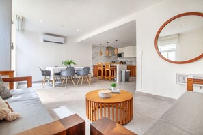 Una sala moderna con una mesa de centro redonda de madera, sofás grises y un comedor con una mesa y sillas blancas.