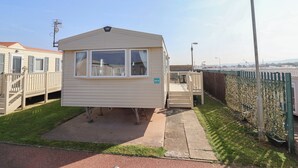 Une maison mobile de plain-pied, dotée d’un petit porche, d’une cour clôturée et offrant une vue sur un ciel dégagé.