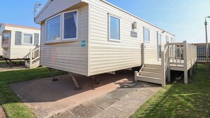 Une maison mobile dotée d’un porche à l’avant, d’une petite terrasse et d’une fenêtre avec des volets.