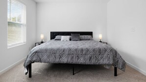 Ein Schlafzimmer mit einem Bett, zwei Nachttischen, einem Fenster mit Jalousien und einem Deckenventilator.