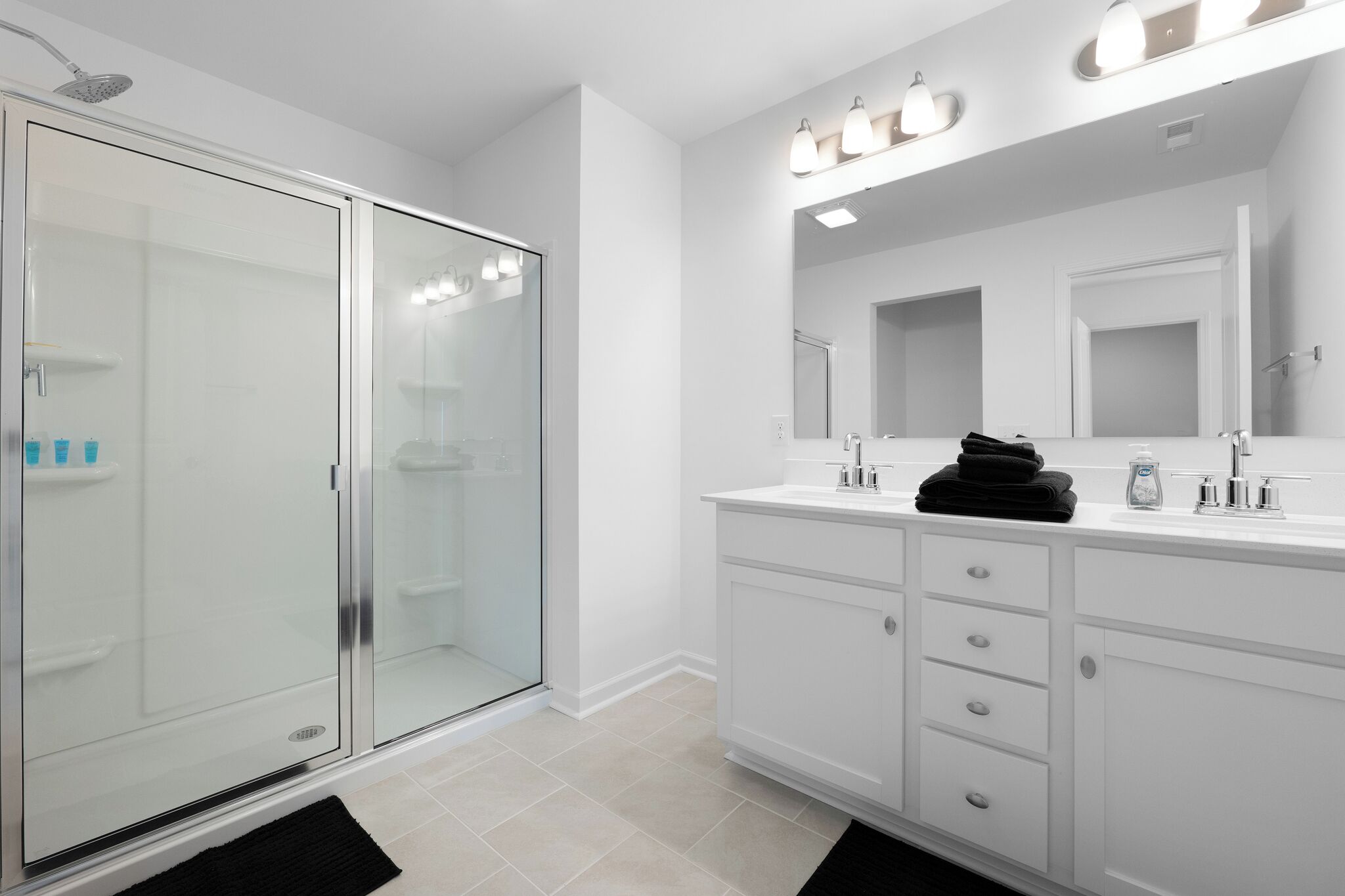 Une salle de bain moderne avec une douche à parois de verre, un grand miroir et des meubles blancs.