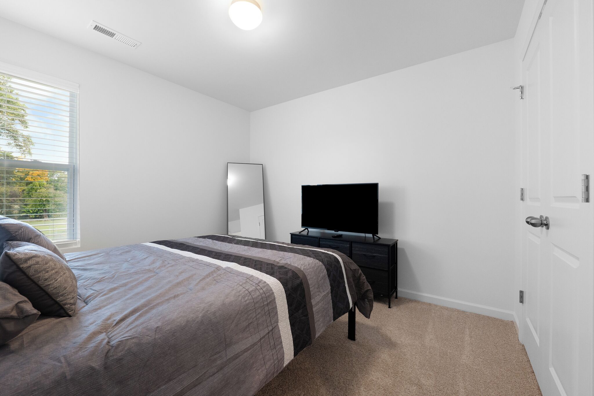 Ein Schlafzimmer mit Bett, Fernseher, Kommode und Tür.