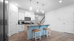 Eine moderne Küche mit weißen Schränken, einer zentralen Kochinsel mit Sitzgelegenheiten, einer Mikrowelle und einer Kaffeemaschine.