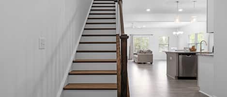 Un interior moderno con una escalera de madera, una zona de cocina y un espacio de sala con un sofá.