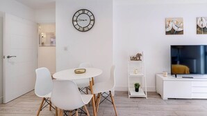 Una sala de estar moderna con comedor, un reloj de pared, obras de arte, un televisor y un mueble blanco.