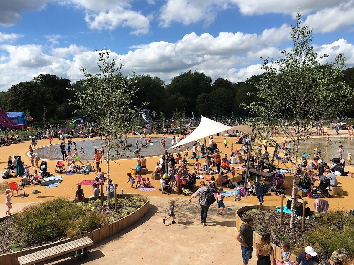 A public park with a sandy play area, benches, and trees.