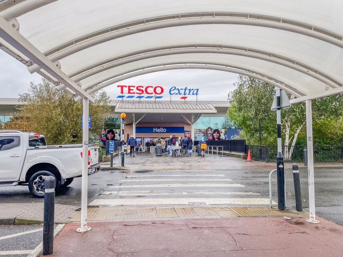 Un magasin Tesco Extra doté d’une entrée couverte, d’une enseigne avec le mot « Bonjour » et d’une voiture visible sur le parking.