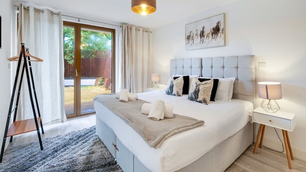 Un dormitorio con una cama grande, una mesita de noche, una lámpara colgante y vistas al exterior.