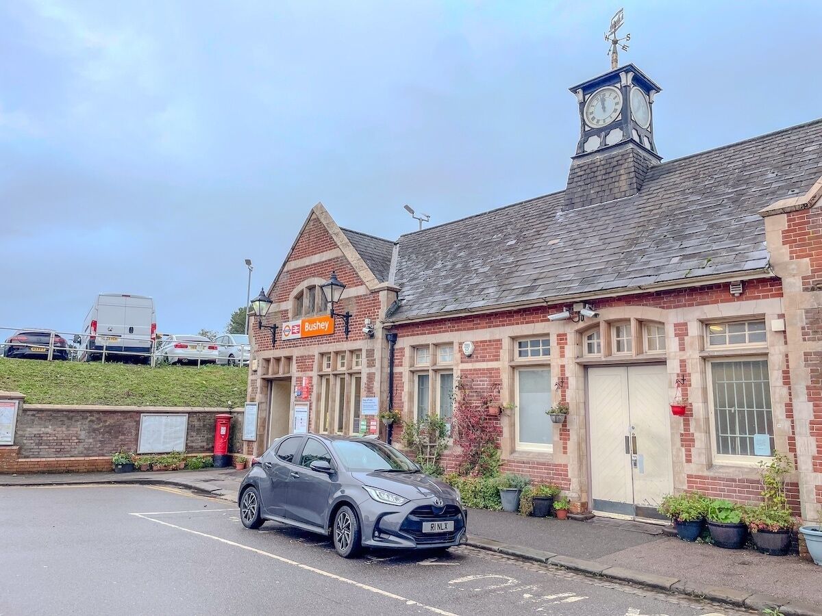 A building with a clock tower, a sign for 'Bushey,' and a parked car.