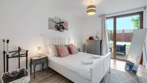 Un dormitorio con cama, mesita de noche, lámpara y vistas al exterior.