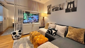 A modern living room with a flat-screen TV, a sofa with patterned cushions, a side table, and a floor lamp. - New Cozy Studio Apartment A (Tampa)