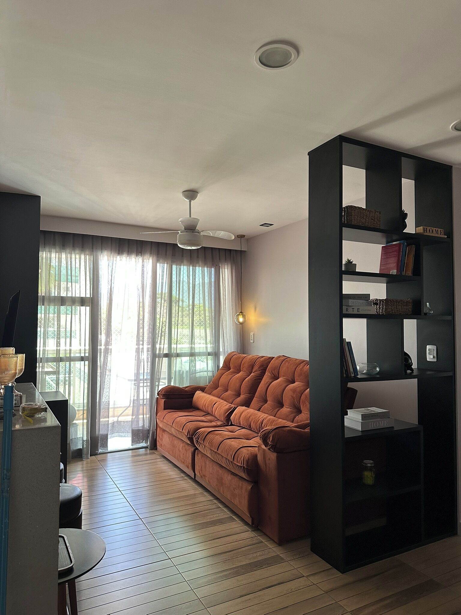 Una sala moderna con un sofá marrón, una estantería negra y un ventilador de techo.