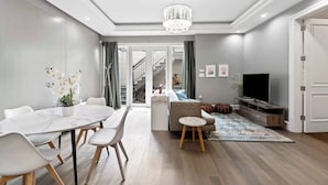 Un soggiorno moderno con zona pranzo, una scala che conduce a un altro livello, televisore e lampadario.