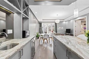 A modern kitchen with a central island, built-in appliances, and a dining area with a chandelier. - Family Guest Suite in Marpole (Vancouver)