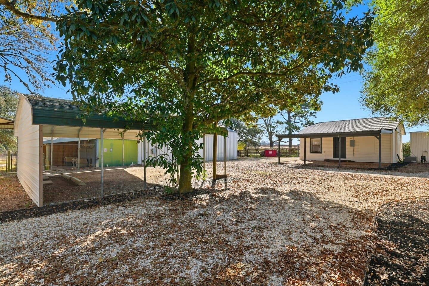 A building with a covered outdoor area, a tree, and a gravel ground.