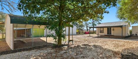 A building with a covered outdoor area, a tree, and a gravel ground.