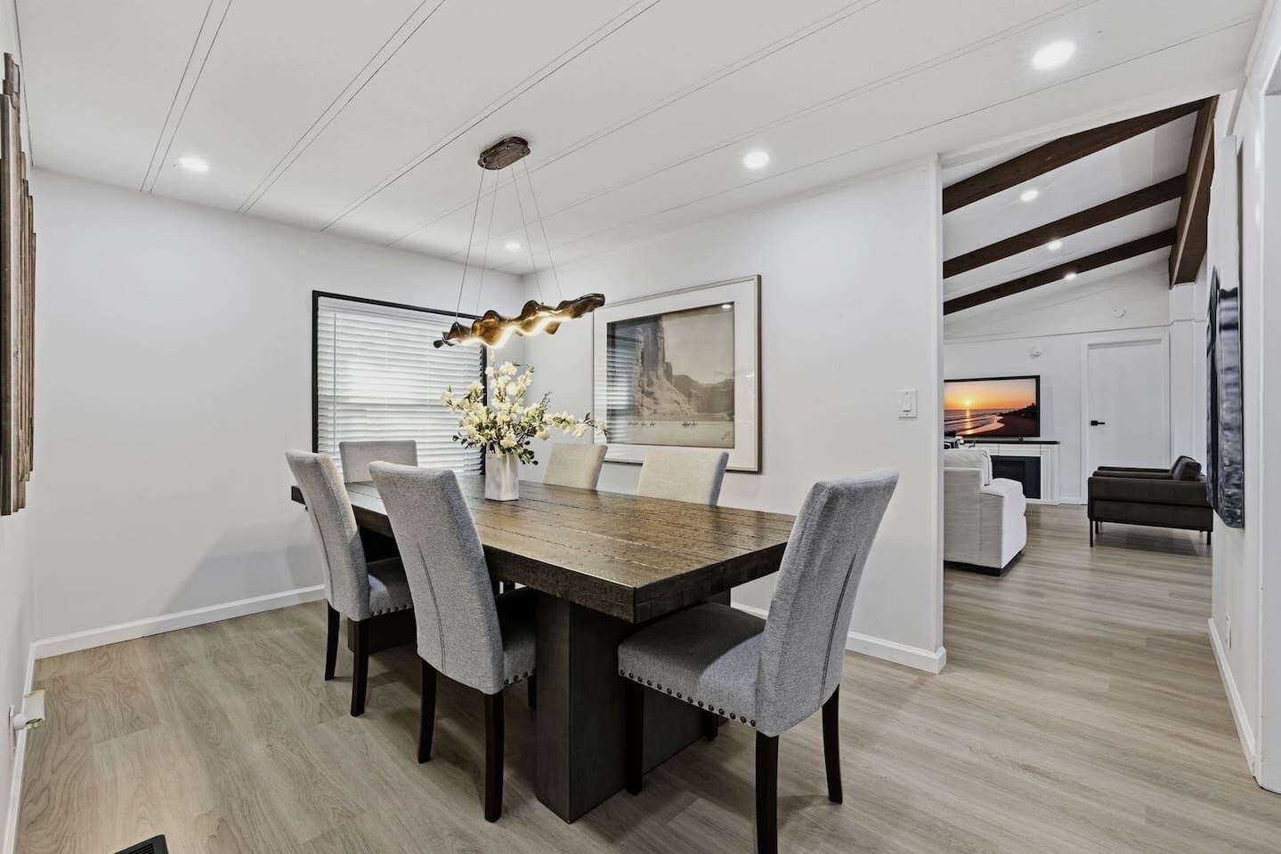 A modern dining area with a wooden table, grey upholstered chairs, and a decorative light fixture.