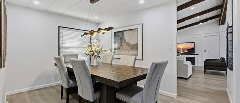 A modern dining area with a wooden table, grey upholstered chairs, and a decorative light fixture.