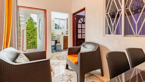 A hotel room with wicker furniture, a dining area, and a view of the garden.