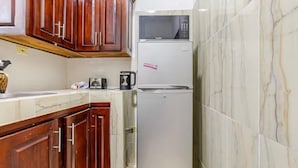 A compact kitchen with wooden cabinets, a microwave, a refrigerator, and a coffee maker.