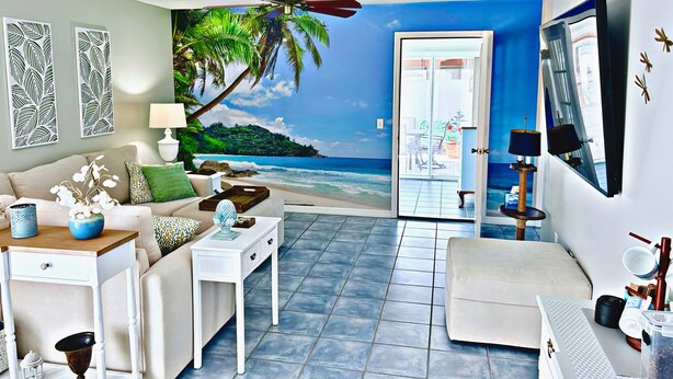 Una sala de estar con un mural de playa, un sofá, una mesa de centro, una mesita auxiliar y una pequeña mesa con adornos.