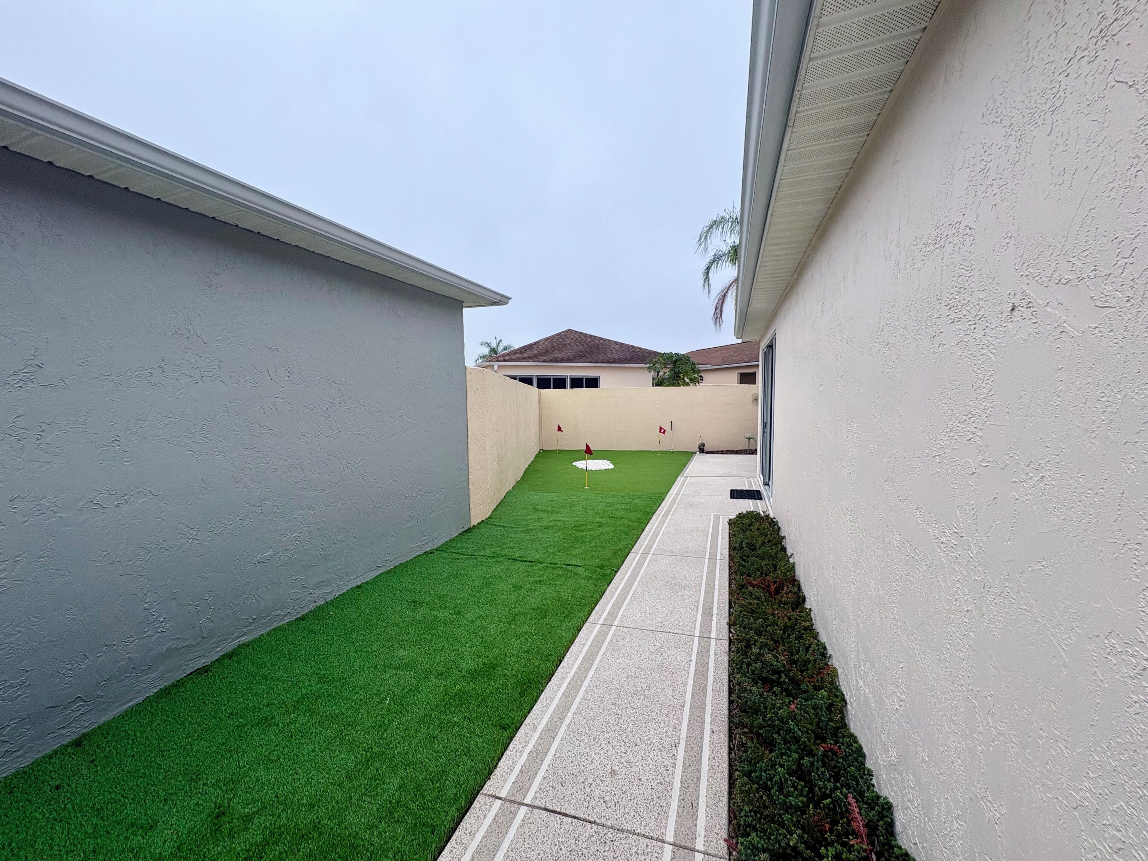 A narrow courtyard with artificial green turf, a concrete pathway, and a white wall.