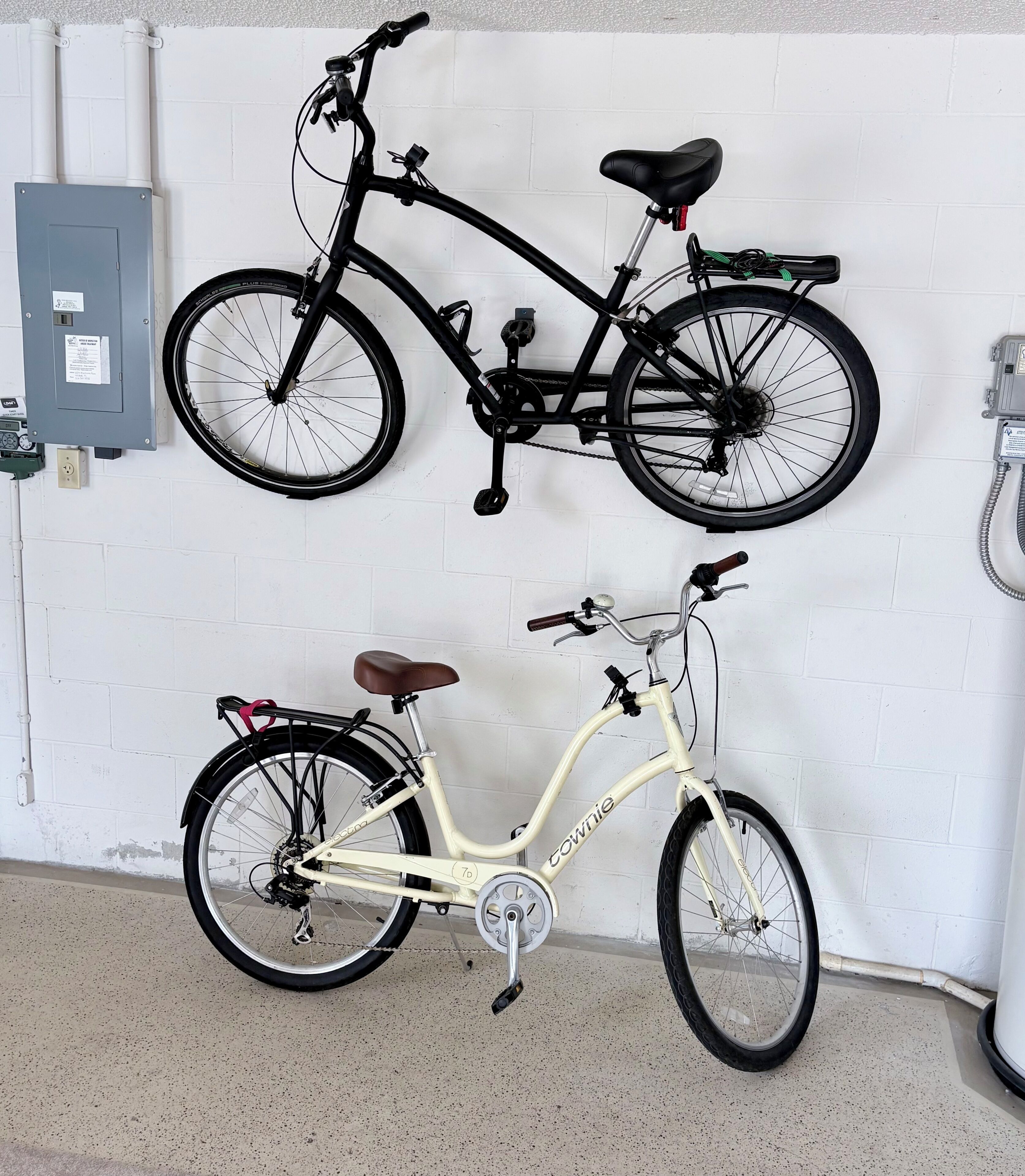 Dos bicicletas colgadas en una pared, un cuadro eléctrico gris y una pared blanca con una puerta.