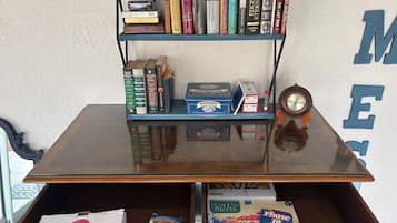 A room with a glass-top table, a bookshelf with books and a magnifying glass, a clock, and a drawer with puzzle boxes.