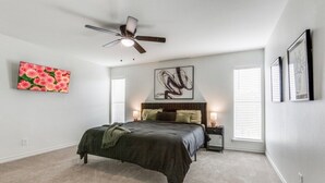 Un dormitorio con cama, ventilador de techo, un cuadro y ventana con persianas.