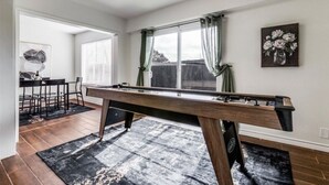 Una mesa de billar en una habitación con comedor y una ventana con cortinas.