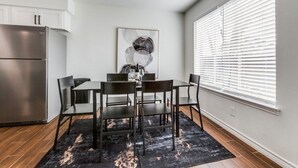 Una cocina moderna con un refrigerador de acero inoxidable, una mesa de comedor con cuatro sillas y un cuadro abstracto en blanco y negro en la pared.