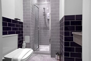 Ein modernes Badezimmer mit barrierefreier Dusche, grauen und schwarzen Fliesen, einer weißen Badewanne und einem weißen Handtuch.
