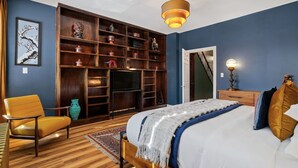 Une chambre à coucher avec un lit, une chaise, un téléviseur, une bibliothèque et une porte.